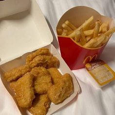 chicken nuggets and french fries in a box on a bed with white sheets