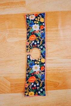 a colorful flowered case with a hole in the middle on a wooden floor next to a pair of scissors