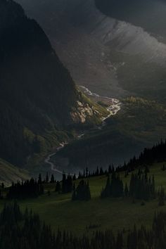 the mountains are covered in green grass and trees, with a river running through them