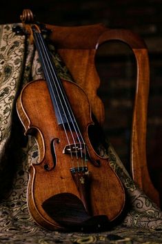 a violin sitting on top of a chair next to a cloth covered bag with an ornate design