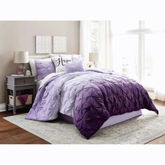 a bed with purple comforter and pillows in a room