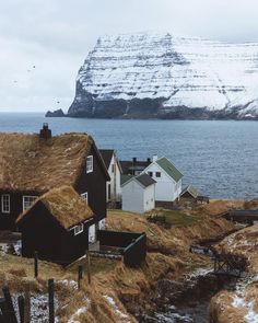 several small houses with grass roofs near the water and snow covered mountains in the background