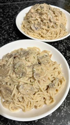 two white plates filled with pasta covered in mushroom sauce on top of a black counter