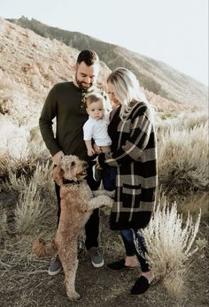 a man and woman holding a baby standing next to a dog