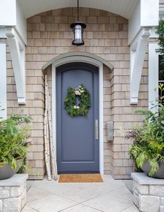 a blue front door with a wreath hanging on it's side and potted plants