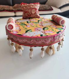 a decorative ottoman with tassels and beads sits on a table in front of a couch