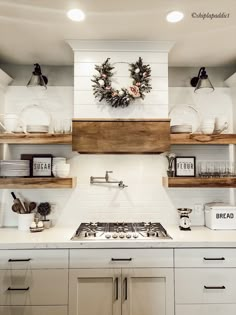 a white kitchen with open shelving above the stove and shelves on the wall, decorated with wreaths