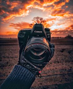 a person holding up a camera with the sun setting in the sky behind them,