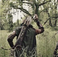 a man with an arrow on his back walking through tall grass in front of trees