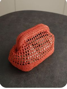 an orange crocheted purse sitting on top of a black table next to a white wall