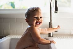 a baby is sitting in the kitchen sink and playing with his hand on the faucet