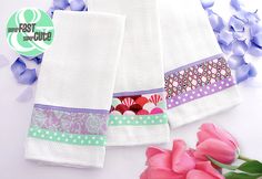 three towels with different designs on them and some flowers in the foreground next to it