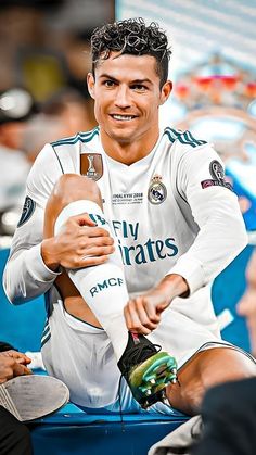 a man sitting on top of a blue bench holding a soccer ball and smiling at the camera