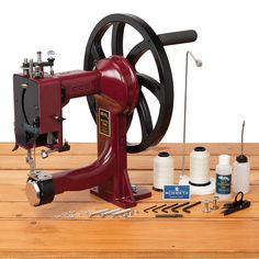 a red sewing machine sitting on top of a wooden table next to threading supplies