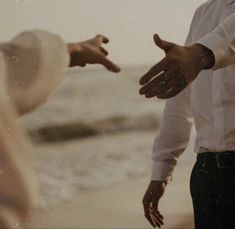 two people standing next to each other with their hands extended out towards the water and one person wearing a hat