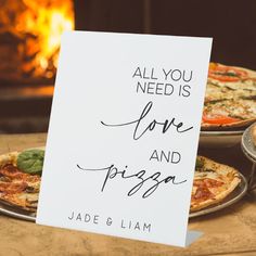 two pizzas sitting next to each other on top of a table with a sign that says, all you need is love and pizza