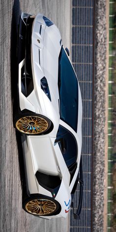 a white sports car with gold rims parked on the side of a road next to a brick wall