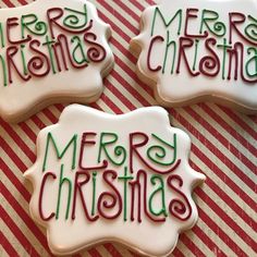 three decorated christmas cookies sitting on top of a red and white striped tablecloth with merry lettering