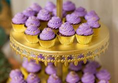 purple cupcakes sitting on top of a gold cake stand