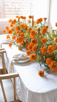 an arrangement of orange flowers in vases on a white table cloth with two chairs