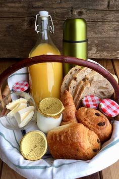 a basket filled with bread and cheese next to a bottle of orange juice on top of a wooden table