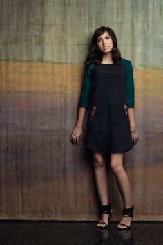 a woman standing in front of a wall with her hands on her hips and looking at the camera