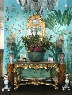 an ornate table with flowers and plants on it in front of a blue wall painted with palm leaves