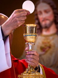 a priest holding a golden chalice in front of a man wearing a red robe