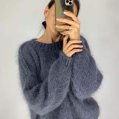 a woman taking a selfie with her cell phone while wearing a fuzzy gray sweater