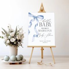 an easel with flowers and eggs on it next to a sign that says welcome to the baby