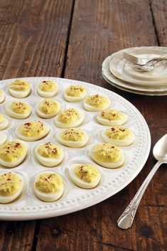 a white plate topped with deviled eggs on top of a wooden table next to silverware