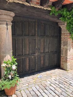 a large wooden garage door sitting on top of a brick sidewalk next to a potted plant