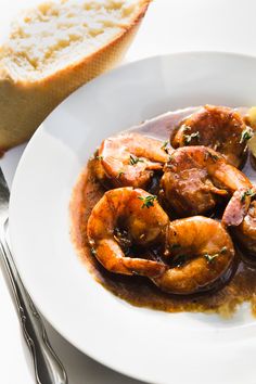 a white plate topped with shrimp covered in gravy next to a slice of bread