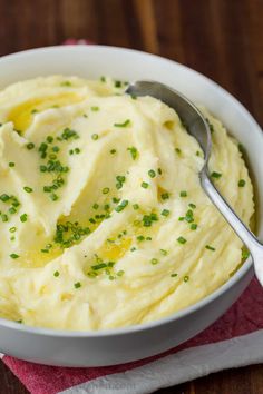 a white bowl filled with mashed potatoes on top of a wooden table next to a fork