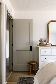 a bedroom with white furniture and a mirror on the wall next to a door that says,