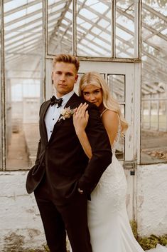 a bride and groom pose for a photo in front of a greenhouse