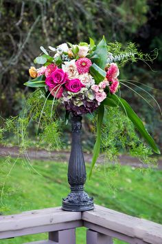 a vase filled with lots of flowers sitting on top of a wooden bench next to a lush green field