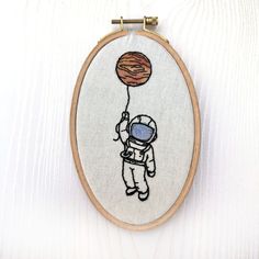 an embroidered wall hanging featuring an astronaut floating with a hot air balloon in his hand