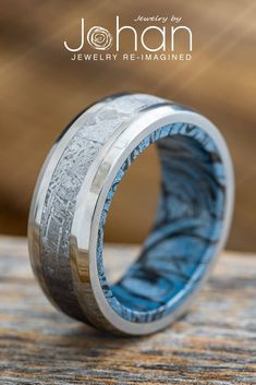 a wedding ring made out of silver and blue inlays, on top of a wooden