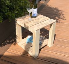 a wooden table with a wine glass and bottle sitting on top of it next to shrubbery