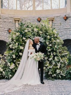 a bride and groom standing in front of a floral arch