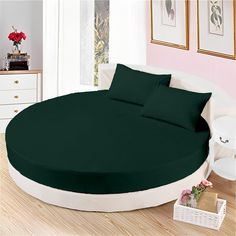 a large round bed with green sheets and pillows on top of it in a room