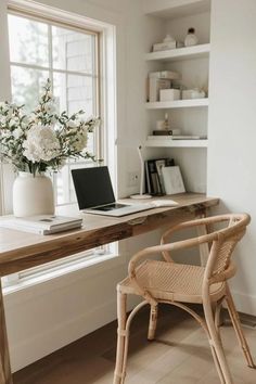 a laptop computer sitting on top of a wooden desk next to a vase with flowers