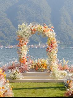 an outdoor ceremony setup with flowers and greenery on the grass by the water's edge