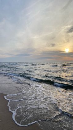 the sun is setting over the ocean with waves crashing onto the beach and sand on the shore