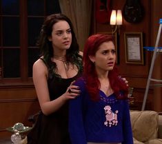 two women standing next to each other in front of a tv screen and one woman with red hair