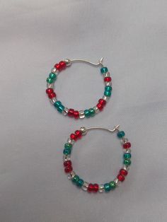 A pair of red, silver lined and green glass seed bead earrings, with a silver 'stopper bead' at the end to stop them easily slipping off the silver hoop.  The hoop has a diameter of approx. 2.3cm. these are quite delicate hoops so care must be taken when putting in and taking out. A fun, festive pair of unique, handmade earrings, with a Christmassy style, ideal for the festive time of year. I can also make in alternative colour combinations if needed, just send me a message with your requirements! To keep your jewellery in the best condition for the longest period, please note:  - Remove jewellery before bathing, showering or swimming.  - Avoid direct contact with body lotions, perfumes and any other chemicals. - Remove jewellery before sleeping. - When not in use, store jewellery in it's Red Christmas Jewelry With Colorful Beads, Festive Beaded Hoop Earrings With Round Beads, Festive Beaded Hoop Earrings, Gift Dangle Hoop Earrings With Spacer Beads, Colorful Beads Christmas Earrings Gift, Colorful Beads Earrings For Christmas Gift, Christmas Gift Earrings With Colorful Beads, Hoop Earrings With Spacer Beads For Gifts, Hoop Earrings With Spacer Beads As Gift