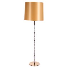 a floor lamp with a gold shade on it's base and a white background