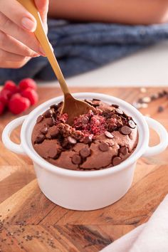 a person scooping chocolate into a bowl with raspberries