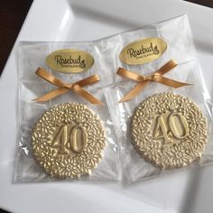 two decorated cookies in plastic wrappers on a white plate with gold ribbon and bow